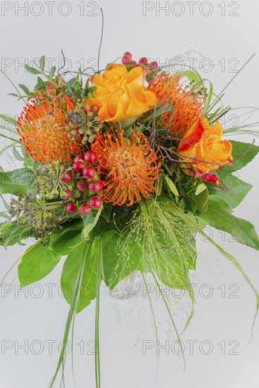 Colorful bouquet in a vase with orange and yellow flowers, red berries and green leaves, protea, roses