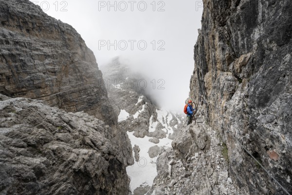 Mountaineer climbs the Via Ferrata Oliva Detassis via ferrata, steep cliffs covered in clouds, Brenta Mountains, Trentino, Italy