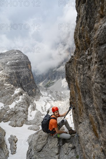 Mountaineer climbs the Via Ferrata Oliva Detassis via ferrata, view of mountain basin with steep cliffs covered in clouds, Brenta Mountains, Trentino, Italy