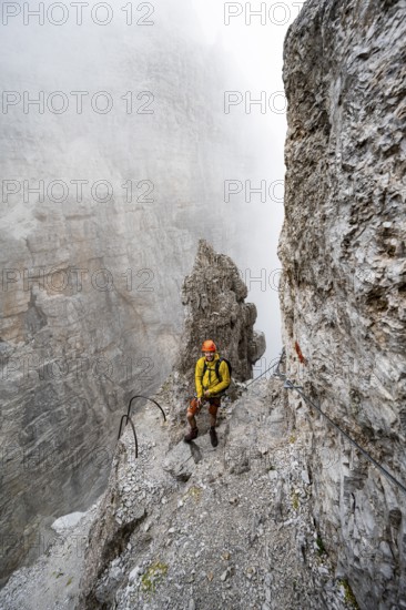Mountaineer climbs the Via Ferrata Oliva Detassis via ferrata in fog, steep mountains covered in clouds, Brenta Mountains, Trentino, Italy