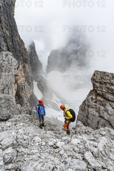 Two mountaineers in rocky, cloudy mountain landscape at Bochetta Bassa del Massodi, Brenta Mountains, Trentino, Italy