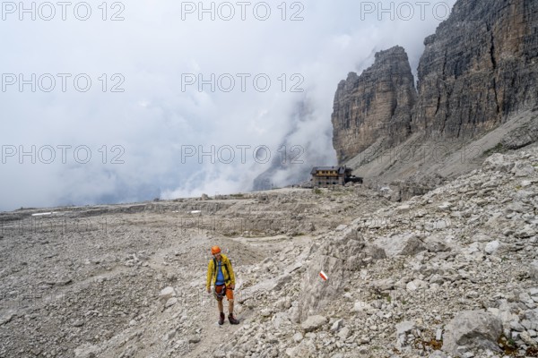 Mountaineers on a hiking trail in a rocky, cloud-covered mountain landscape while descending to Rifugio Alimonta, Brenta Mountains, Trentino, Italy