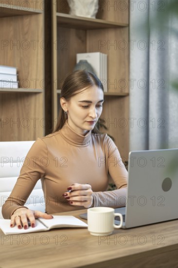 Woman working at wooden desk with laptop and notebook in calm home office