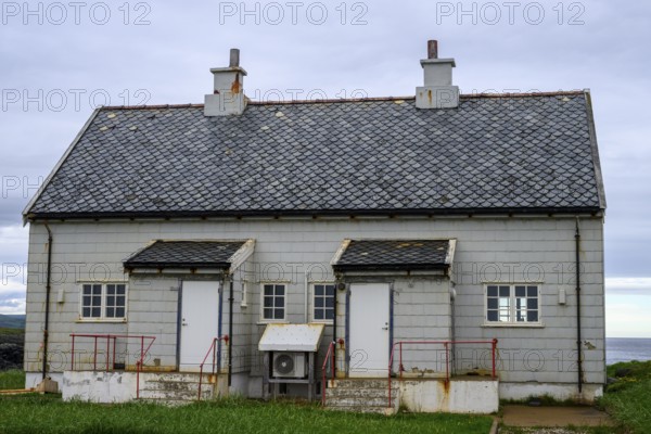 An old grey lighthouse dictionary house with a sloping roof at Kjølnes Fyr, small windows and railings in a rural area, Berlevåg, Finnmark, Norway
