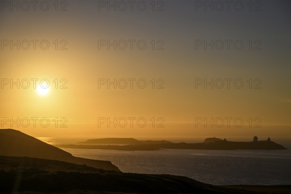 Midnight sun on Mount Domen in the background the city of Vardø, sea at sunset with golden sky and calm atmosphere, Kiberg, Finnmark, Norway
