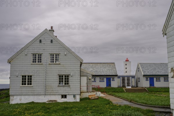 Lighthouse between blue and white houses rises under a grey sky Kjølnes Fyr, small windows and railings in a rural area, Berlevåg, Finnmark, Norway