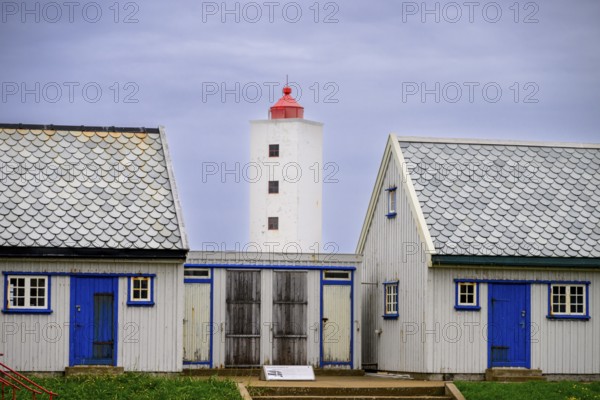 Lighthouse between two blue and white houses rises under a grey sky Kjølnes Fyr, small windows and railings in a rural area, Berlevåg, Finnmark, Norway
