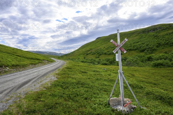 A lonely road with a road sign in a green hilly landscape under a partial sky, Berlevåg, Finnmark, Norway