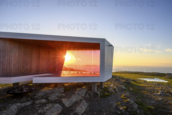 Modern building with glass wall in front of sunset on Mount Domen, sea view, nestled in rocky landscape, Kiberg, Finnmark, Norway