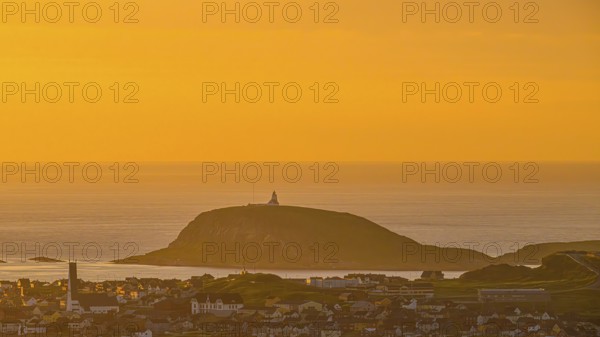 View of the city of Vardø from Mount Domen in the background the island of Hornoya with the lighthouse, sea at sunset with golden sky and calm atmosphere, Kiberg, Finnmark, Norway