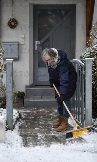 Elderly woman with broom, sweeping week, cleaning, sweeping snow, sidewalk, sidewalk, snowfall, snow, winter, Stuttgart, Baden-Württemberg, Germany