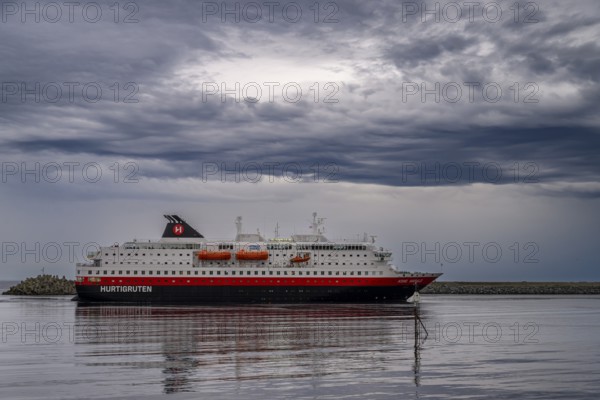 The Hurtigrouten Hurtigruten ship Kong Harald arrives at Berlevag harbour, on the horizon with a cloudy sky, Berlevåg, Finnmark, Norway