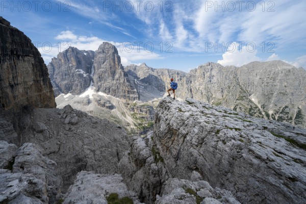 Mountaineers on a rock in front of picturesque mountain landscape with rocky peaks, Via Ferrata SOSAT via ferrata, summit of Cima Tosa in the back, Brenta Mountains, Trentino, Italy