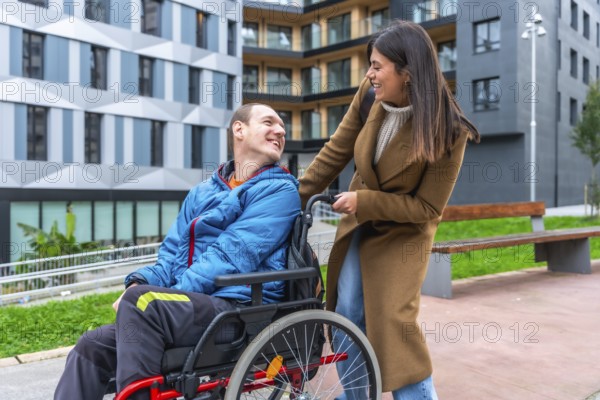 Woman companion assisting a smiling man using a wheelchair, enjoying a happy moment together in an urban park setting, representing support, accessibility, and inclusion