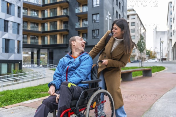Man with a disability in a wheelchair laughing happily while a female caregiver pushes him along a modern urban street, demonstrating joy and inclusion