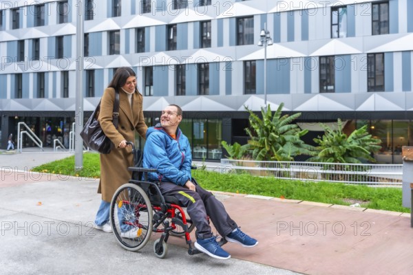Happy woman caregiver pushing smiling adult man in a wheelchair on an accessible ramp in an urban environment, promoting concepts of support, mobility, and inclusion