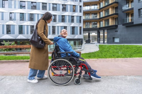 Caregiver pushing a happy adult man with a disability in a wheelchair, enjoying time outdoors together in an urban environment with modern buildings in the background