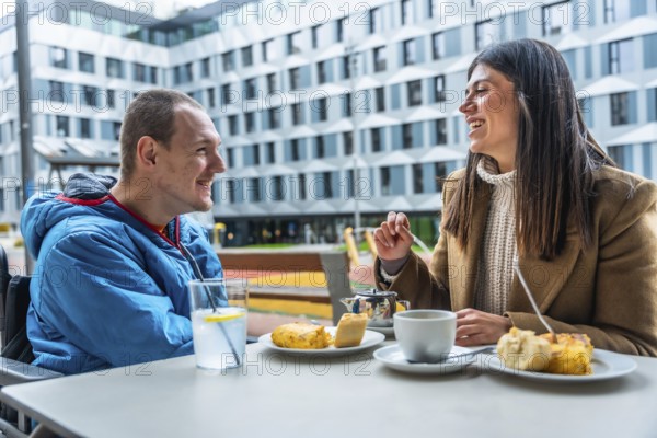 Young man in wheelchair having a joyful conversation and enjoying coffee with a female friend at an outdoor cafe, symbolizing inclusion, friendship, and happy social interaction