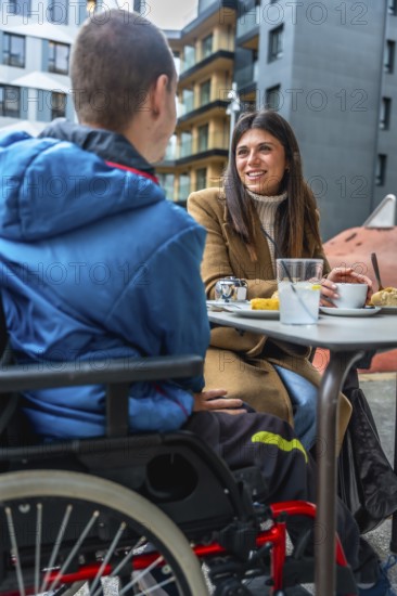 Woman and boy with disabilities enjoying a conversation together while sitting at an outdoor cafe table in an urban setting, sharing an inclusive moment
