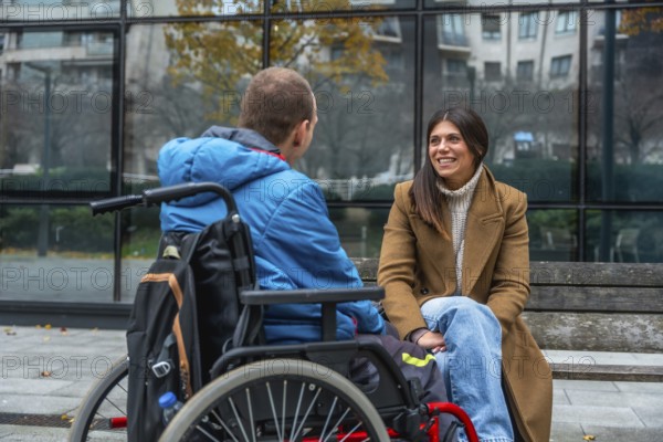 Disabled man seated in a wheelchair engaging in a joyful conversation with a supportive woman on a bench, fostering inclusion and social connection outside