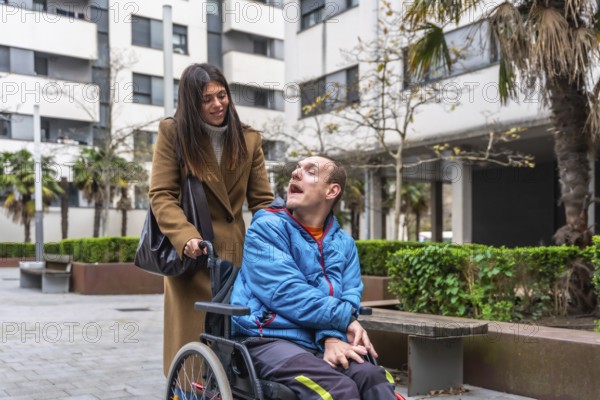 Woman pushing an adult man in a wheelchair, providing support and care during an urban outing, emphasizing challenges and inclusion for people with disabilities
