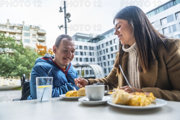 Smiling caregiver offering food to a man in a wheelchair, enjoying a pleasant conversation and meal together at a city cafe, symbolizing support, inclusion, and everyday social life