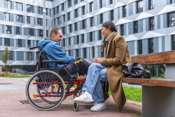 Man in a wheelchair and woman sitting on a bench engaging in a friendly conversation outdoors, promoting concepts of connection, active listening, and social inclusion