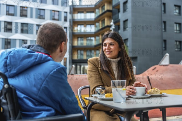 Woman and boy in a wheelchair share a warm, engaged conversation at an outdoor urban cafe, smiling and connecting through supportive, inclusive companionship and communication