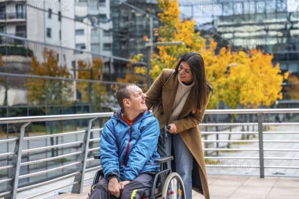 Support worker assisting a smiling disabled man in a wheelchair on an autumn day, navigating an accessible urban environment with modern buildings and colorful trees