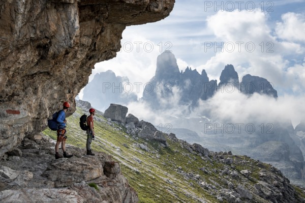 Two mountaineers on a path in front of a picturesque mountain landscape with rocky peaks, Via Ferrata SOSAT via ferrata, Cima Tosa summit in the back, Brenta Mountains, Trentino, Italy