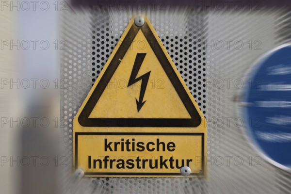 (Photo montage) Text CRITICAL INFRASTRUCTURE on a warning sign for a high-voltage line