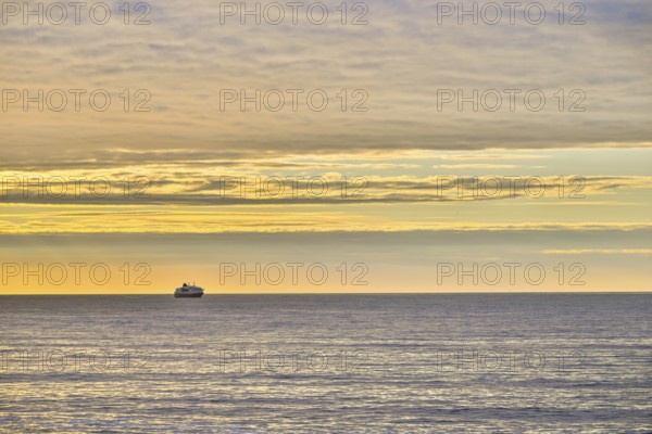 A Hurtigrute ship on the wide Barents Sea at sunset midnight sun, yellowish clouds and calm seas, Berlevåg, Finnmark, Norway