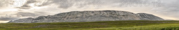 A massive granite rock mountain with bare fells dominates the landscape of the central Varanger Peninsula at Austertanaveien 890 in the foreground, green low fells vegetation wide, quiet landscape, Tana, Finnmark, Norway