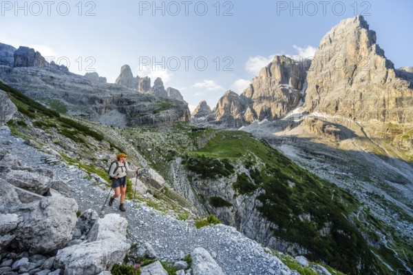 Female mountaineer hiking on a hiking trail in front of picturesque mountain scenery in the morning, Rifugio Ai Brentei mountain hut and Cima Tosa rock summit, Brenta, Trentino, Italy