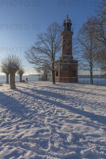 Holtenau lighthouse at the entrance of the Kiel Canal in winter, west bank of the Kiel Fjord, shipping, brick building from 1895, round tower, orientation, sea sign, beacon, ground floor with wedding room, trees, snow, blue sky, Baltic Sea, Kiel, Germany