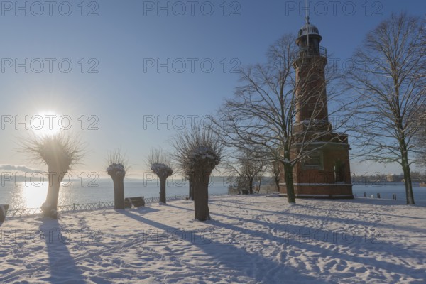Holtenau lighthouse at the entrance of the Kiel Canal in winter, west bank of the Kiel Fjord, shipping, brick building from 1895, round tower, orientation, sea sign, beacon, ground floor with wedding room, trees, snow, blue sky, back light, sun, Baltic Sea, Kiel, Germany