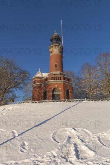 Holtenau lighthouse at the entrance of the Kiel Canal in winter, west bank of the Kiel Fjord, shipping, brick building from 1895, round tower, orientation, sea sign, beacon, ground floor with wedding room, trees, hills, snow, blue sky, Baltic Sea, Kiel, Germany