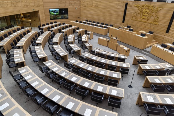 Plenary hall deserted with the seats of deputies and the government bank. Behind it is the coat of arms of the federal state. The state parliament of Baden-Württemberg is the state parliament based in Stuttgart, Baden-Württemberg, Germany