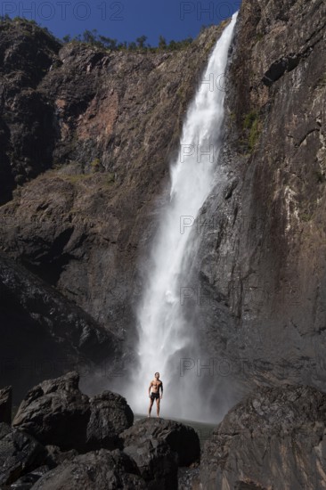 Daytime scene at Wallaman Falls with a fit man in swim trunks below the waterfall, Queensland, Australia
