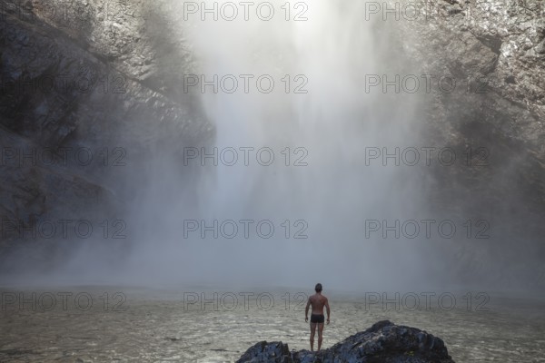 Daytime scene at Wallaman Falls with a fit man in swim trunks below the waterfall, Queensland, Australia