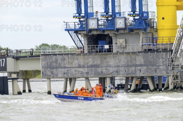 THW lifeboat with crew in orange clothing sails in front of port facilities on rough water, Wilhelmshafen, Jadebusen, Lower Saxony, Germany