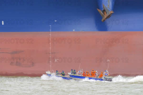 THW lifeboat with crew in orange clothing sails in front of a large ship hull on rough water, Wilhelmshafen, Jadebusen, Lower Saxony, Germany