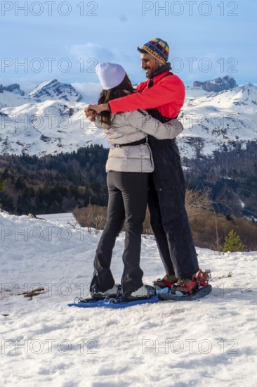 Happy couple embracing each other while snowshoeing on a snowy mountain landscape, enjoying a romantic winter adventure and a healthy outdoor lifestyle in nature