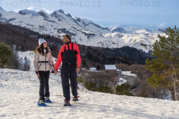 Couple snowshoeing hand in hand through fresh pyrenees snow, smiling and enjoying a sunny winter hiking adventure together on a scenic mountain trail