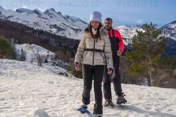 Couple snowshoeing side by side through fresh deep snow in the pyrenees on a sunny winter day, enjoying outdoor adventure, fitness and togetherness in a scenic mountain landscape