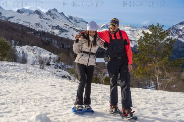 Happy couple engaging in active winter outdoor recreation, snowshoeing on a snowy mountain landscape, supported by a partner as they learn and enjoy the adventure