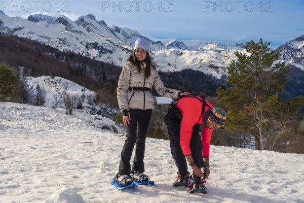 Couple adjusting gear with snowshoes on a snow covered mountain slope, preparing for winter hiking and enjoying outdoor recreation under a clear blue sky