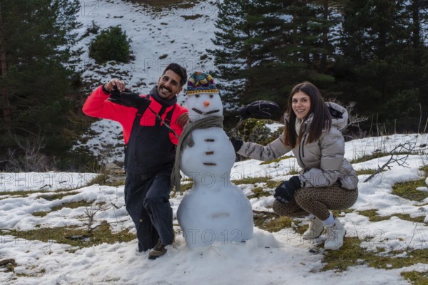Couple building a snowman together on a snowy mountain slope, smiling and bundled in winter gear, enjoying friendship, outdoor fun and a frosty holiday day