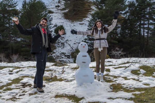 Smiling couple posing with a freshly built snowman during winter vacation, celebrating connection, friendship, and joy while embracing the cold weather and outdoor fun activities