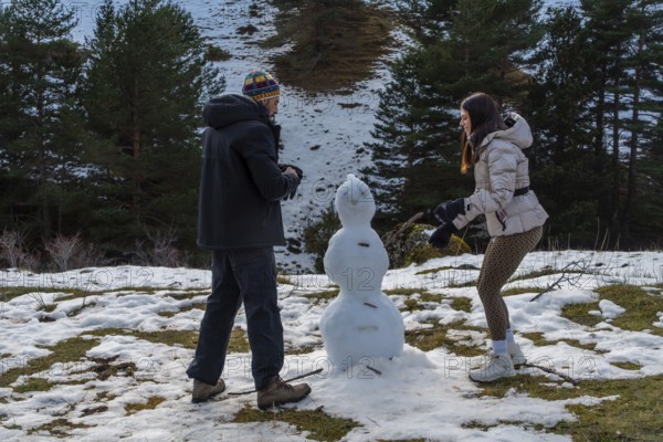 Couple building a snowman outdoors on a snowy hillside, wearing warm winter clothing and enjoying a fun recreational activity during an active weekend in nature